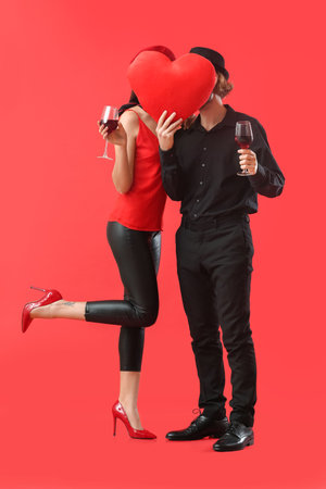 Happy young couple with wine and red heart on color background. Valentine's Day celebrationの写真素材