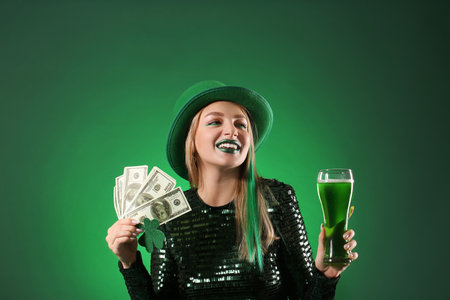 Beautiful woman with dollar banknotes and glass of beer on green background. St. Patrick's Day...