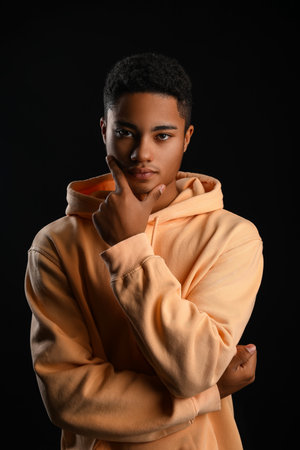 Portrait of African-American teenage boy in hoodie on black backgroundの写真素材