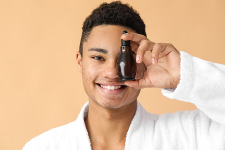 Young African-American guy with serum for skin care on color background