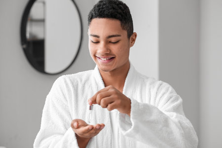 Young African-American guy using serum for skin care in bathroomの写真素材