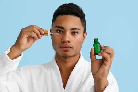 Young African-American guy with serum for skin care on color backgroundの写真素材