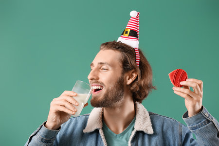 Handsome man with gingerbread cookie drinking milk on green backgroundの写真素材