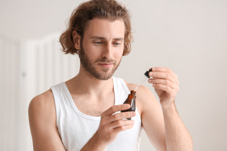 Young man using serum for skin care in bathroom