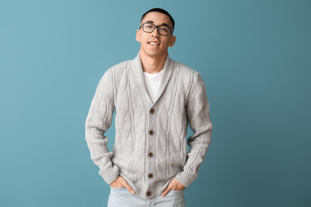 Handsome young Asian man in knitted sweater on blue backgroundの写真素材