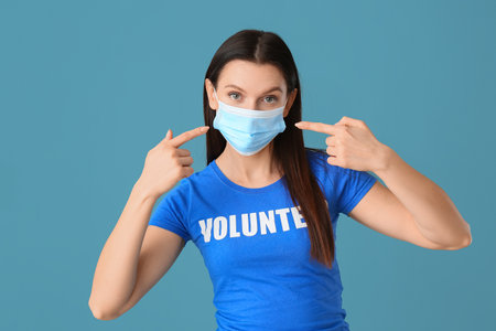 Female volunteer pointing at medical mask on blue backgroundの写真素材