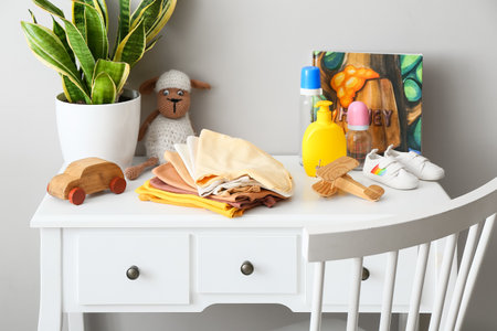 Baby clothes with toys, bottles and houseplant on table near light wallの写真素材