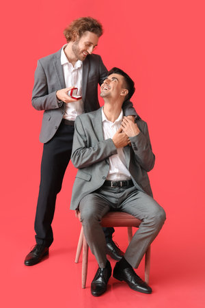 Young gay proposing to his boyfriend on red backgroundの写真素材