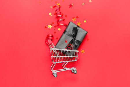 Shopping cart with gift box and confetti on red background. black friday saleの写真素材