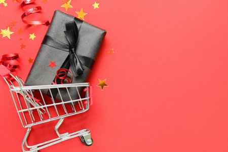 Shopping cart with gift box and confetti on red background. black friday saleの写真素材