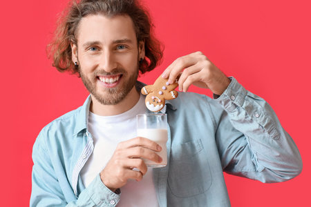 Happy young man with Christmas cookie and glass of milk on red background, closeupの写真素材