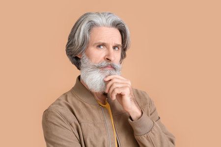 Thoughtful senior man in stylish jacket on beige background