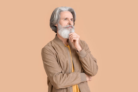 Thoughtful senior man in stylish jacket on beige background