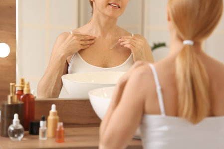 Mature woman using cosmetic serum in bathroomの写真素材