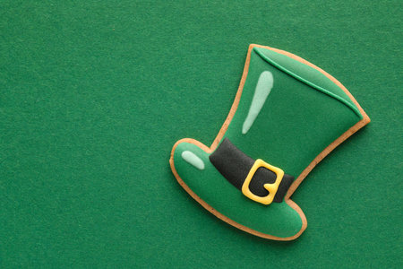 Tasty gingerbread cookie in shape of hat for St. Patrick's Day celebration on green backgroundの写真素材