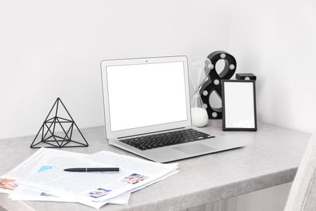 Modern laptop, newspapers and blank photo frame on table near light wallの写真素材