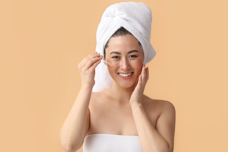 Young Asian woman with cosmetic serum on beige backgroundの写真素材