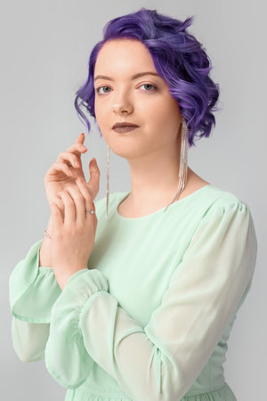 Beautiful young woman with violet hair on light background. Very Peri - color of year 2022