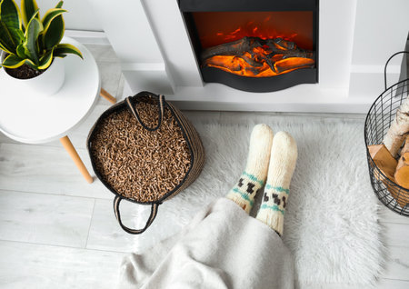 Bag with wood pellets and woman warming near fireplace in living roomの写真素材