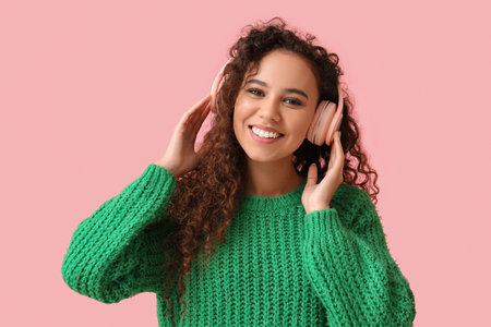 Young African-American woman in headphones listening to music on pink backgroundの写真素材