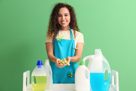 Young African-American woman with table, clothespins and bottles of detergent on green backgroundの写真素材
