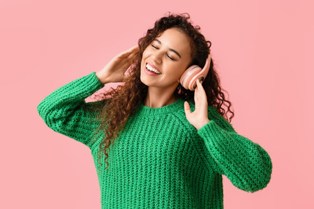 Young African-American woman in headphones listening to music on pink backgroundの写真素材