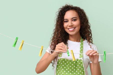 Young African-American woman hanging clothespins on color backgroundの写真素材