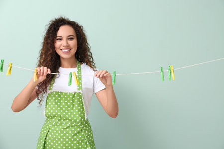 Young African-American woman with hanging clothespins on color backgroundの写真素材