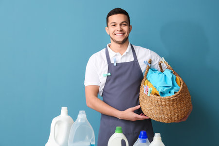 Young man with laundry basket, clothespins and bottles of detergent on blue backgroundの写真素材