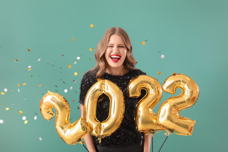 Beautiful young woman with balloons in shape of figure 2022 on color background. new year celebrationの写真素材