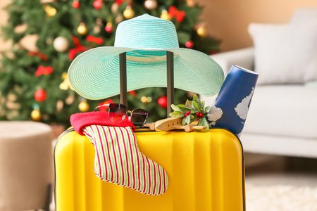 Hat with Christmas sock, wooden airplane, mistletoe and world map on yellow suitcase in roomの写真素材