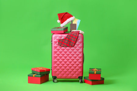 Pink suitcase with Christmas gift boxes, sock, passport and Santa hat on green backgroundの写真素材