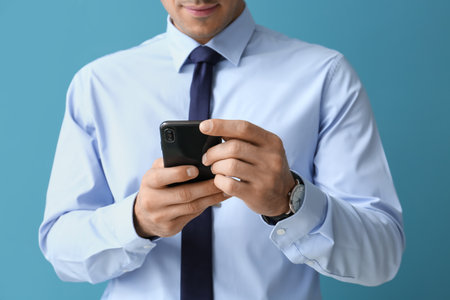 Handsome man in formal clothes using mobile phone on color background, closeupの写真素材