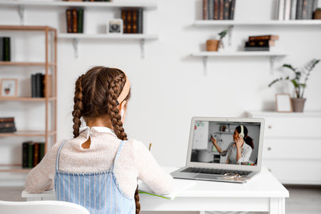 Little girl in earphones studying with online tutor at home, back viewの写真素材