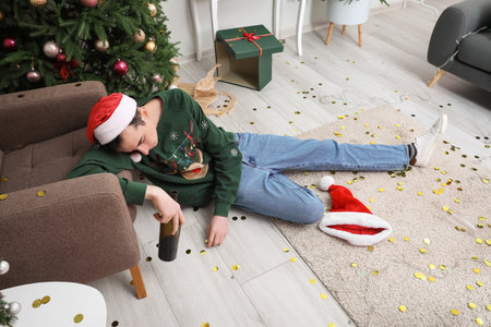 Drunk young man with empty bottle sleeping after Christmas party at homeの写真素材