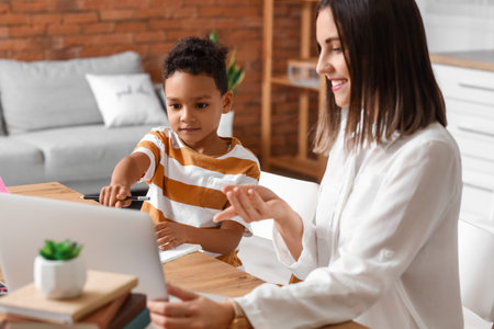 Little African-American boy pointing at laptop while studying with tutor at homeの写真素材