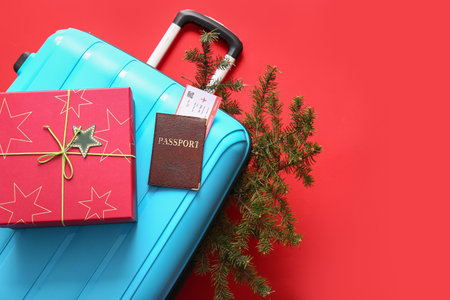 Suitcase, gift box, documents and fir branch on red background, closeup. christmas vacation conceptの写真素材