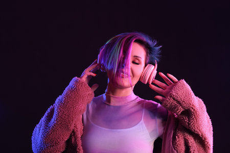 Beautiful woman with unusual hair listening to music on black background