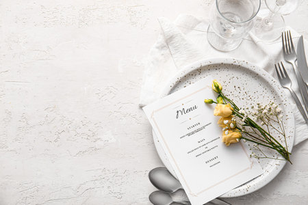 Beautiful table setting with menu and flowers on light backgroundの写真素材