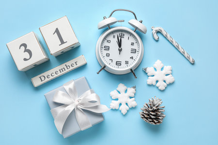 Cube calendar with date 31 DECEMBER, vintage alarm clock, Christmas decor and gift on blue...