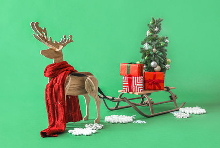 Wooden reindeer with scarf, sledge, Christmas tree and presents on green backgroundの写真素材