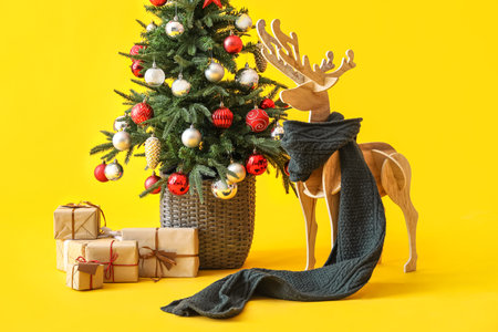 Wooden reindeer with scarf, Christmas tree and presents on yellow backgroundの写真素材