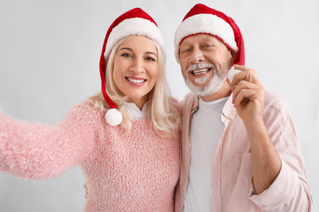 Happy mature couple in Santa hats taking selfie on light backgroundの写真素材