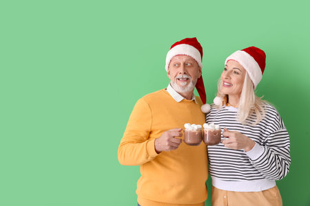 Happy mature couple in Santa hats and with hot chocolate on color backgroundの写真素材