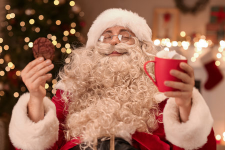 Santa Claus with cup of hot cocoa and cookies in room on Christmas eveの写真素材