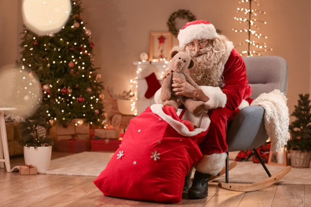 Santa Claus taking teddy bear from bag in room on Christmas eveの写真素材