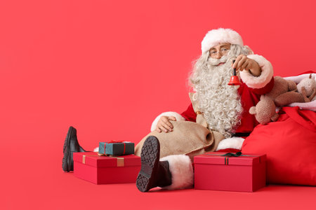 Santa Claus with Christmas bell, bag and gift boxes on red backgroundの写真素材