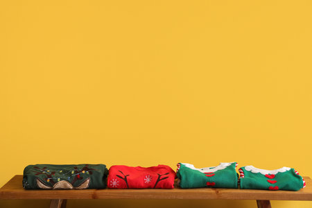 Bench with folded Christmas clothes on color background
