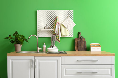 Wooden counter with silver sink, cookware, houseplant and pegboard near green wall in kitchenの写真素材