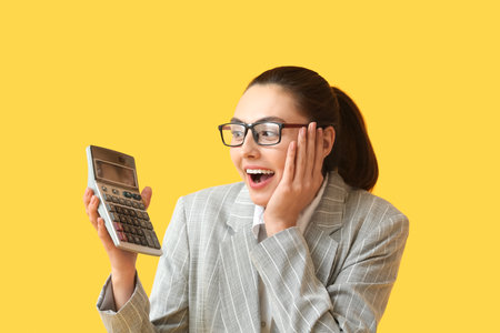 Surprised young businesswoman with calculator on yellow backgroundの写真素材